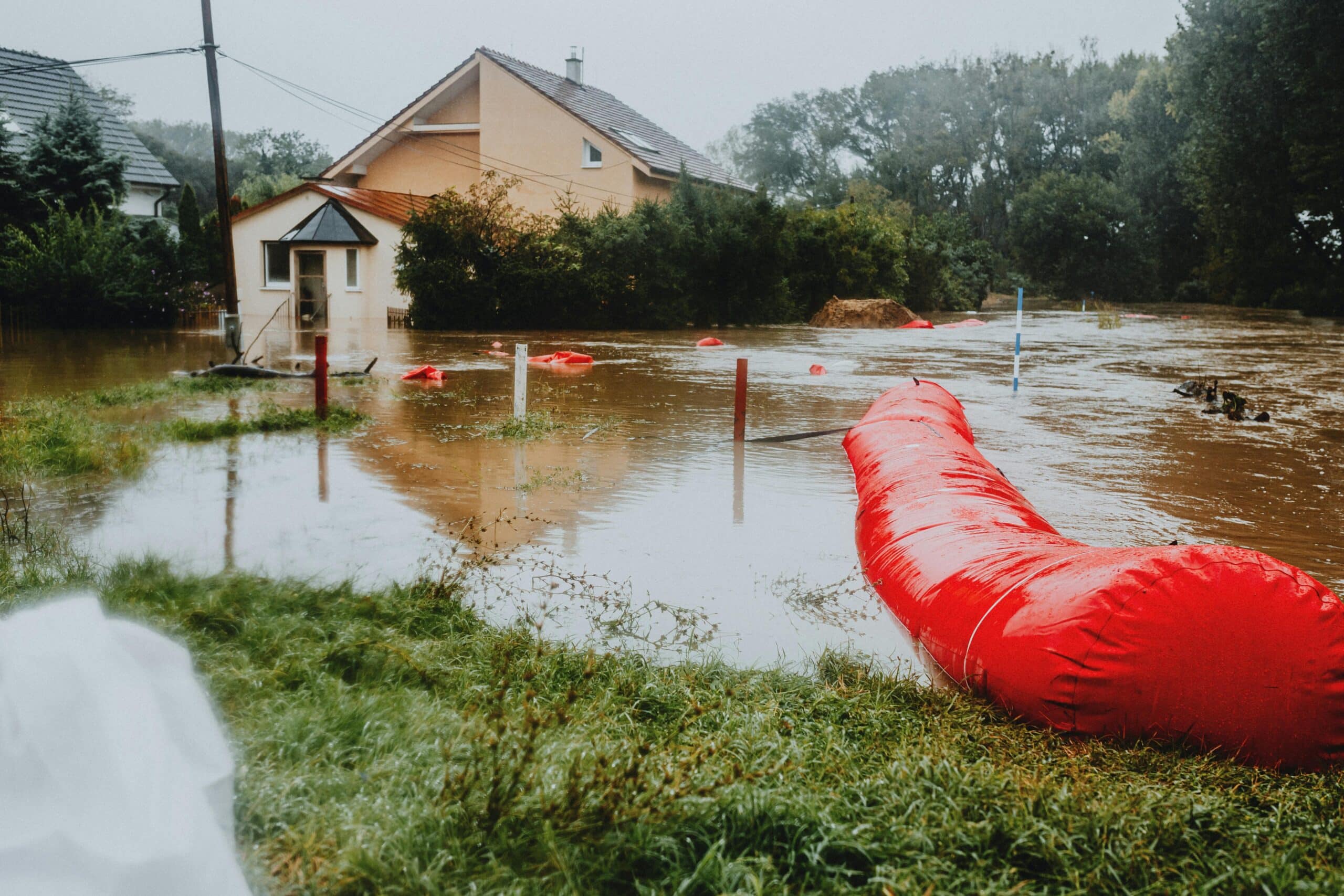 Hochwasserschutz Regensburg Ein überschwemmtes Wohngebiet, das durch rote Hochwasserschutzbarrieren geschützt ist und die Auswirkungen des Unwetters deutlich macht.