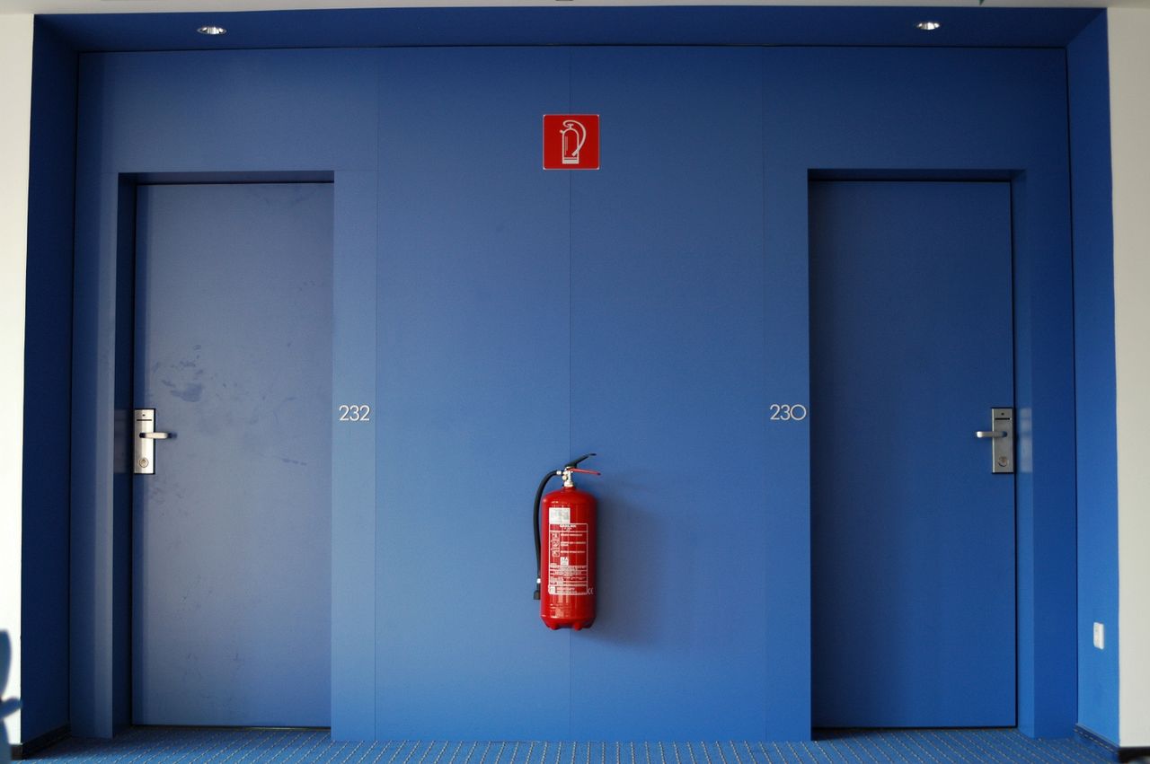 Brandschutz in Industrie: Blaue Türen in einem Flur, zwischen denen ein roter Feuerlöscher steht. 